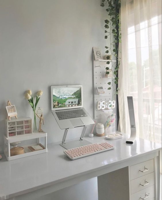 a white study space with a laptop on a stand, some stands for organizing, a pegboard with a clock and potted greenery