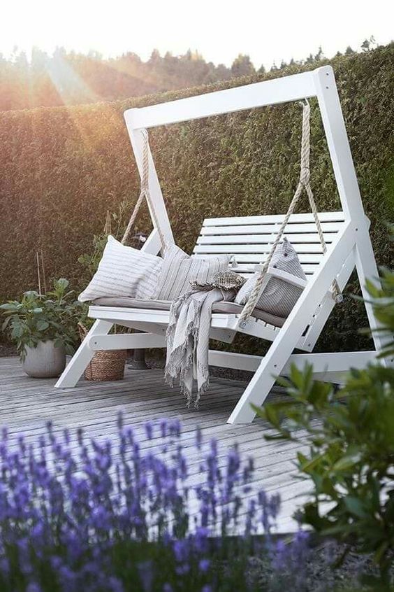 a white swinging bench with pillows and potted greenery around are a great combo for a modern terrace or patio