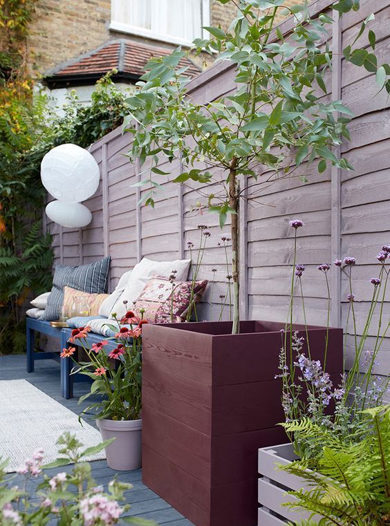 a whitewashed wooden fence, a navy bench with pillows, potted trees and blooms for a cozy and welcoming backyard