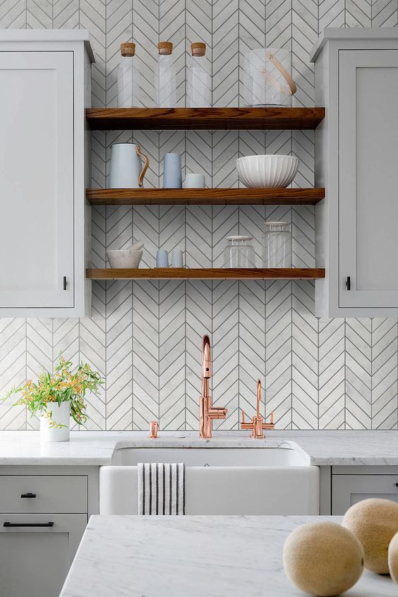 an elegant dove grey kitchen with marble chevron tiles on the backsplash, stained shelves and some tableware