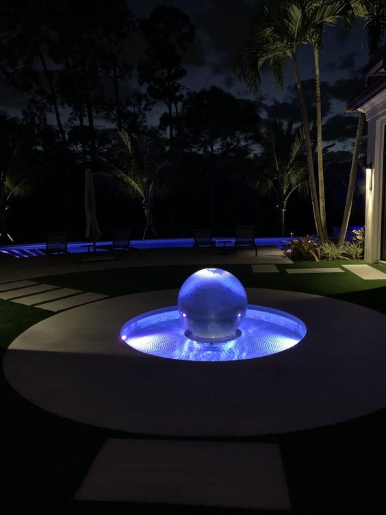 an ultra-modern water feature clad with tiles, with a lit up glass sphere in the center as a water and light decoration for a garden