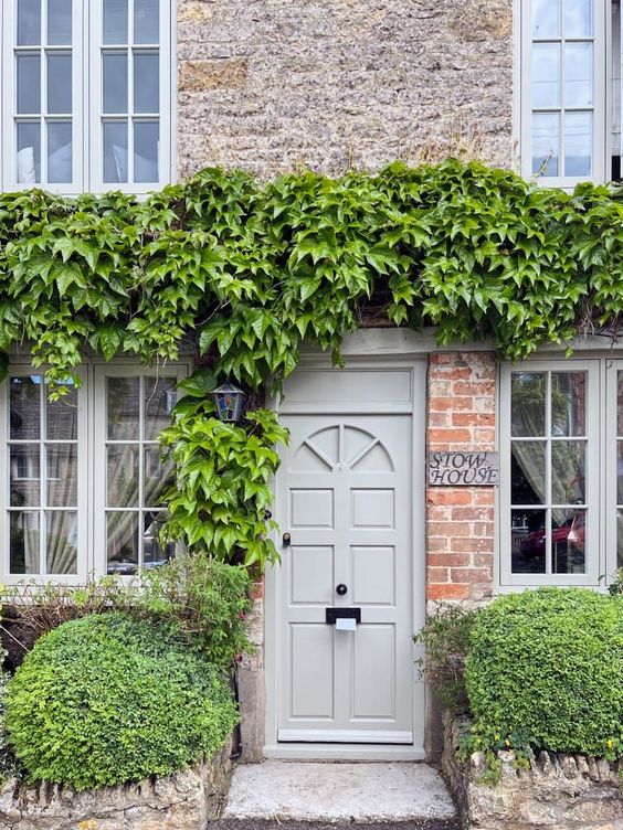 Potted boxwood topiaries, lush green climbers over the door refresh the red brick exterior walls and add interest to them. 