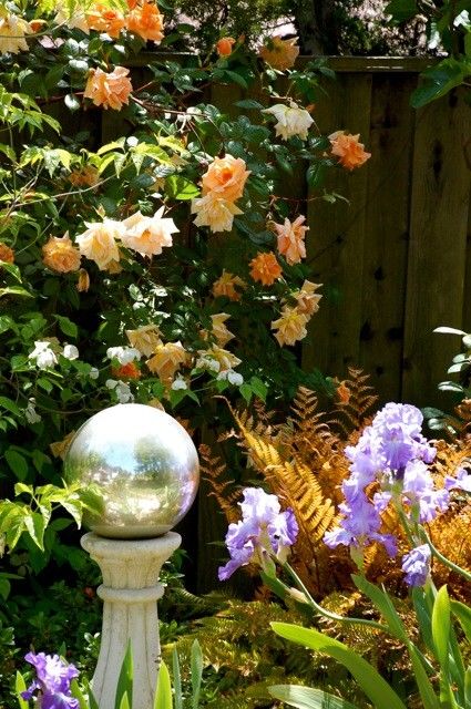 bright blooms and leaves, a silver garden ball on a stone stand create a beautiful arrangement for an outdoor space