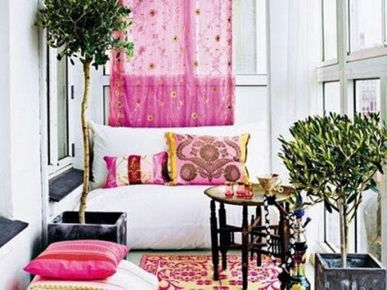 a boho colorful balcony with a bright rug, colorful pillows, a white loveseat, potted trees, a Moroccan side table and a view