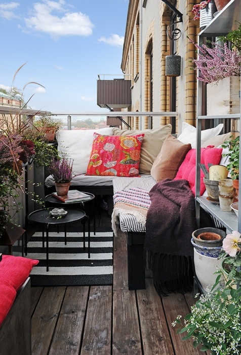 a bold boho balcony with a striped corner sofa with colorful pillows, lots of potted greenery and blooms around feels relaxed and free-spirited