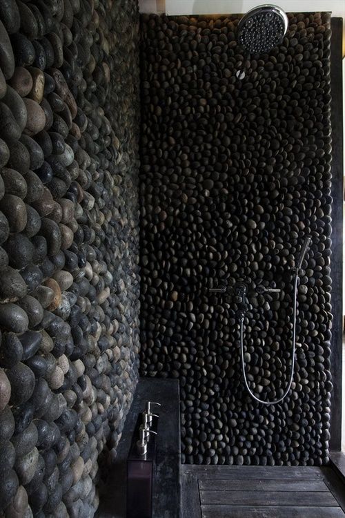 a beautiful and refined shower clad with black pebble,s with a wooden floor and a black stone console is a dramatic and chic idea