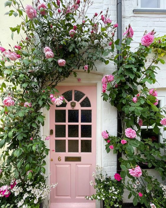 A pink door is echoed with bright pink flourishing vines going around it to make the front porch look cuter