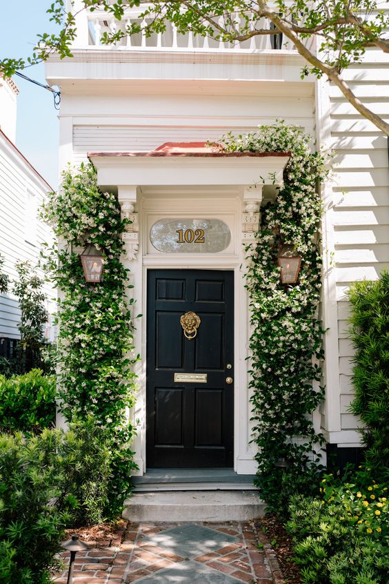 A classic elegant black door with gold touches is refreshed with bold green and white flower vines on both sides of the door.