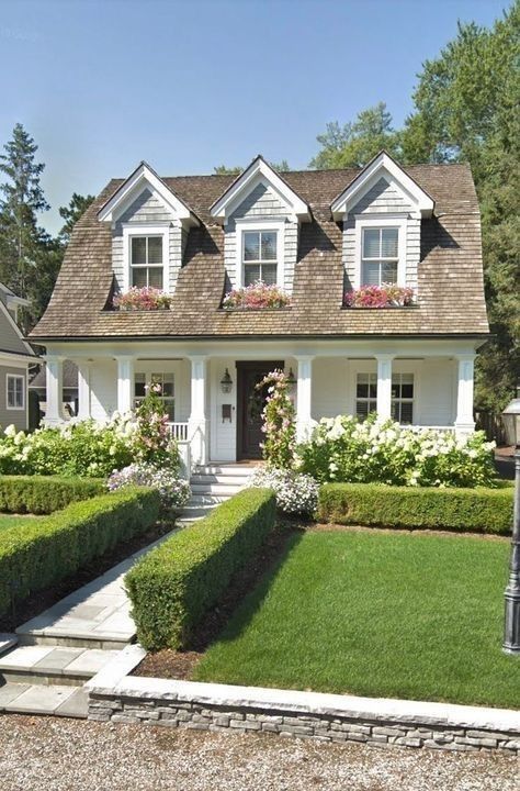 Manicured front yard with a green lawn, green walls and white blooms along the house to create a perfect cottage look.
