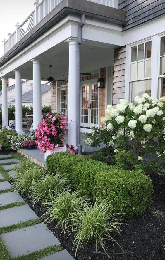 Flower beds along the house and on both sides of the porch with greenery and blooms are a cool idea for a refined modern front yard. 