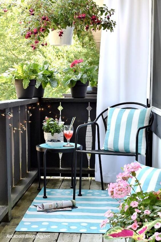 light blue printed pillows and a rug and potted pink flowers turn this balcony in a light inviting space