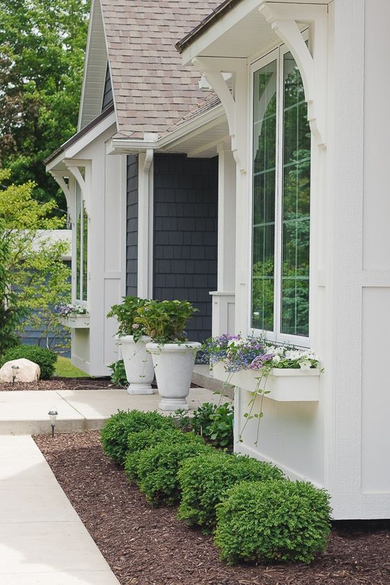 Simple garden beds along the house, with topiaries, potted greenery on the porch and window boxes with blooms refresh the exterior of the house and its front yard.