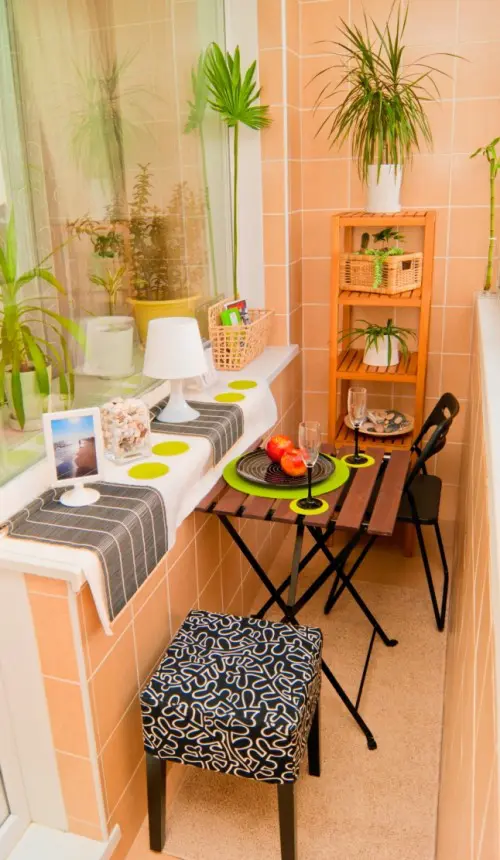 a small and cozy balcony with a shelf, a windowsill table, a couple of chairs and some potted plants