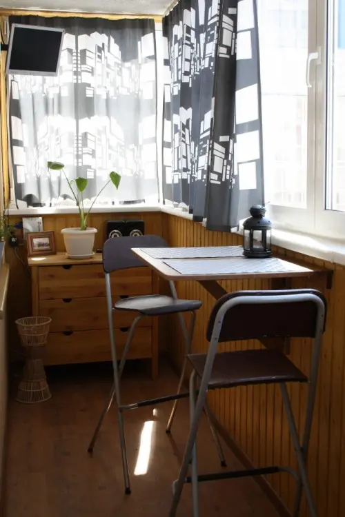 a small balcony with curtains, potted plants and some folding furniture is a cool space to have a meal, a drink or do some work