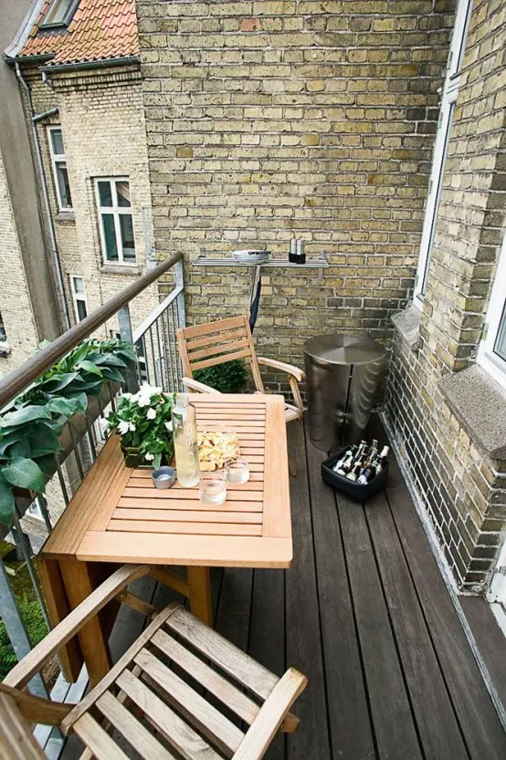 a cozy balcony with a folding table and some chairs, greenery and decor will make you feel like in the countryside due to lots of wood used