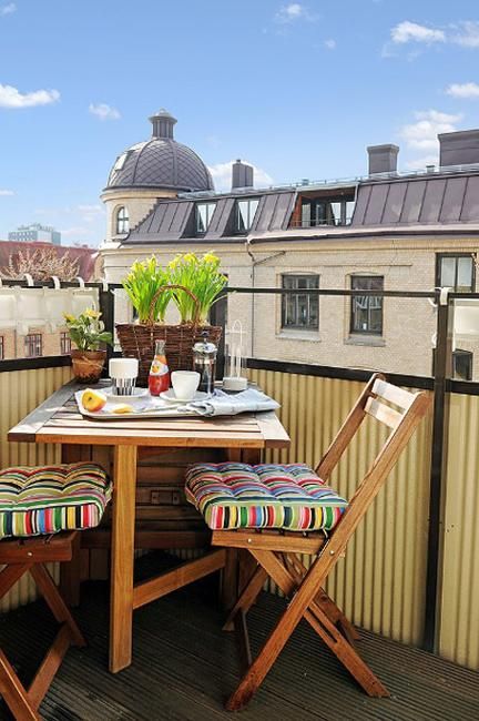 a tiny balcony with folding furniture and potted greenery, bright cushions and towels is a lovely space to have a meal or a drink