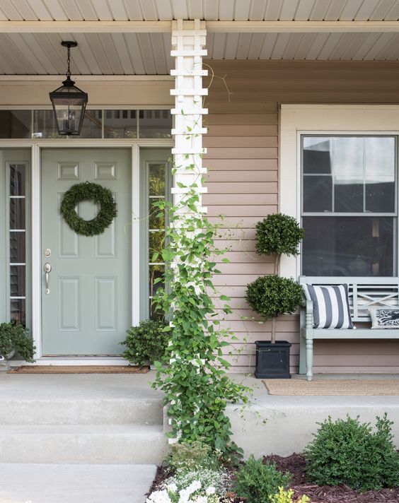 A beautiful cottage porch with green climbers going up the pillar, with topiaries and a green wreath to refresh the space.