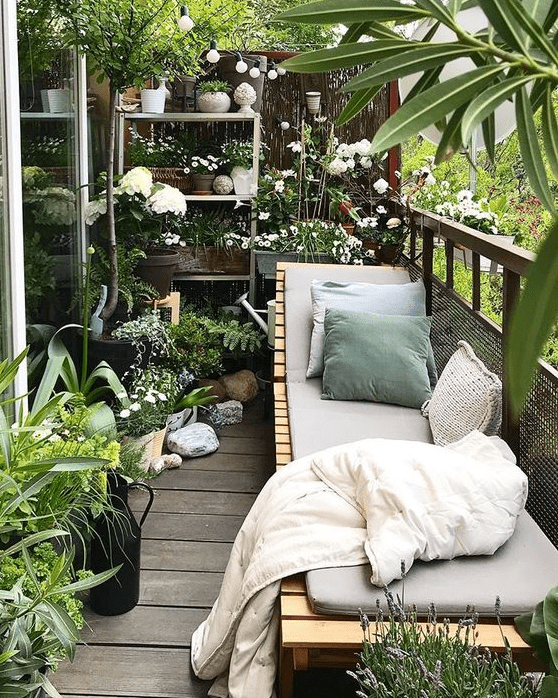 a balcony garden with potted greenery and blooms and a wooden lounger with upholstery and pillows is a gorgeous place to be