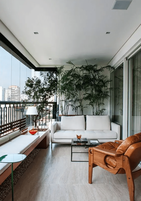 a chic and bold modern balcony as an outdoor living room, with potted plants, a white sofa and an upholstered bench, a wood and leather chair and bright accents