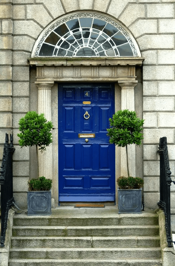 a chic vintage entrnace with a bold blue door with gold details, concrete planters with topiary trees for an accent