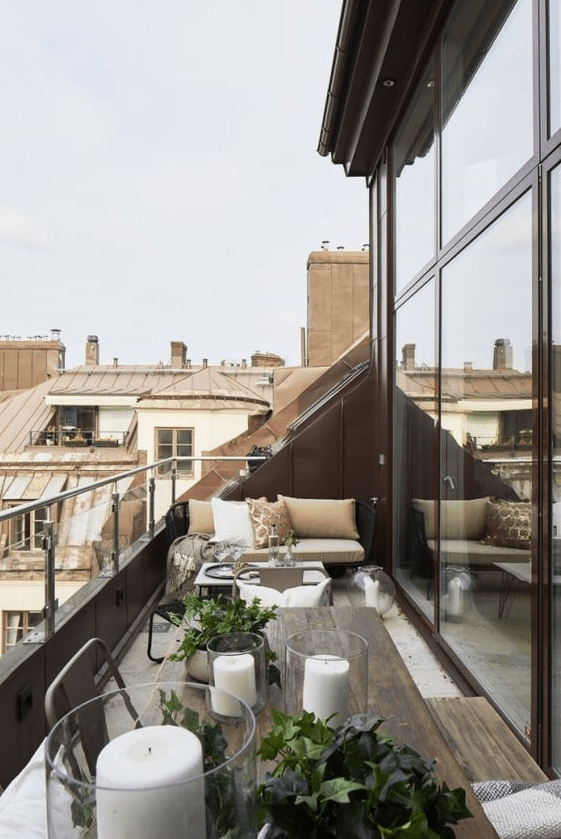 a contemporary blacony with dark metal and wooden furniture, candle lanterns, greenery and some printed and plain textiles