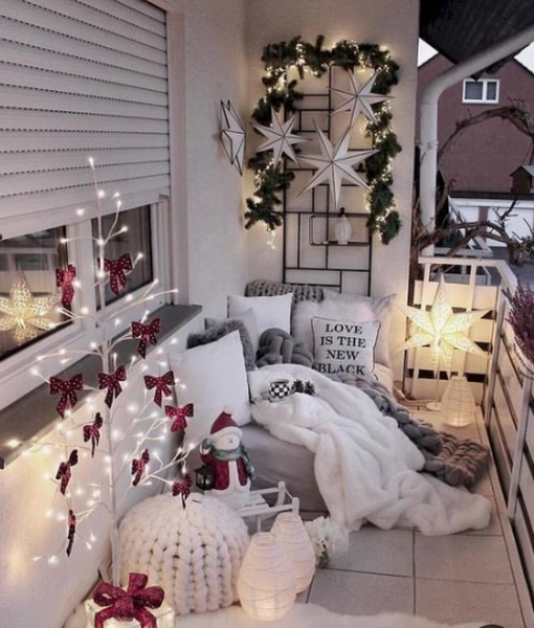 a cozy little balcony with a light tree with red bows, some candle lanterns, a star lamp, stars and greenery on the wall and fur and knit textiles