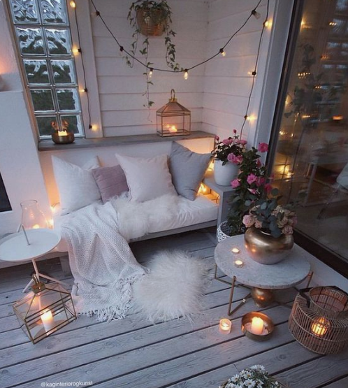 a cozy winter balcony with faux fur, candles in lanterns and candleholders, lights and potted blooms