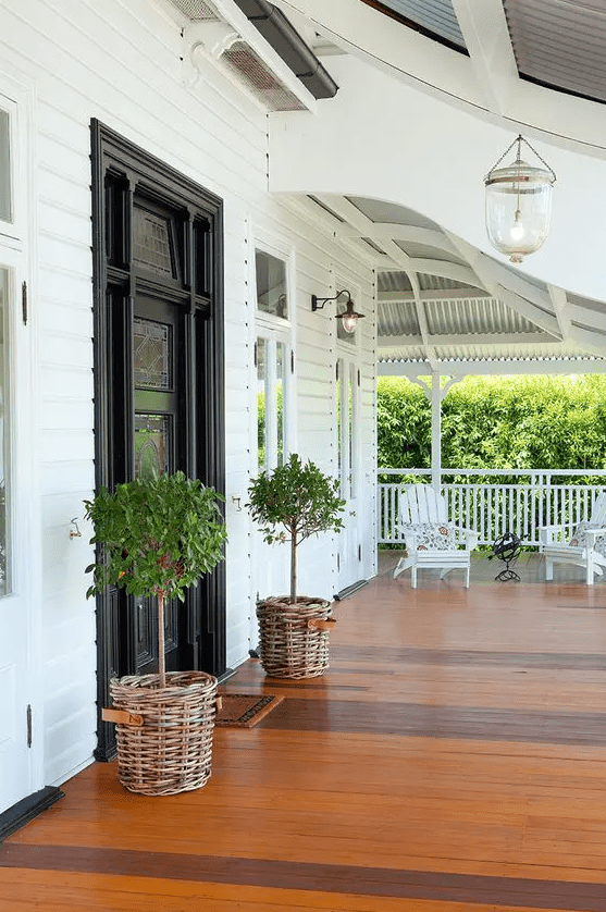 a farmhouse porch with a black door with mosaic glass and topiaries in basket planters is a lovely and cozy space