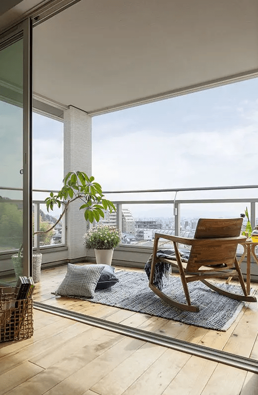 a laconic modern balcony styled with a wooden rocker, a side table and some pillows and potted plants is a cool space