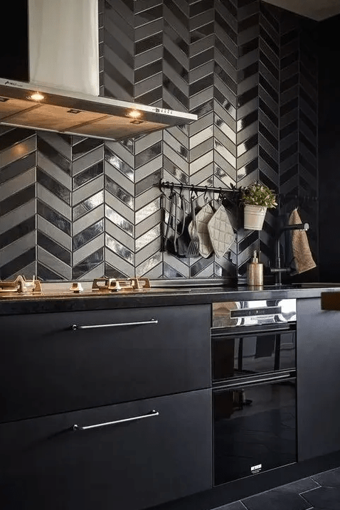 a matte black kitchen with black countertops and a shiny and matte chevron tile backsplash plus black countertops