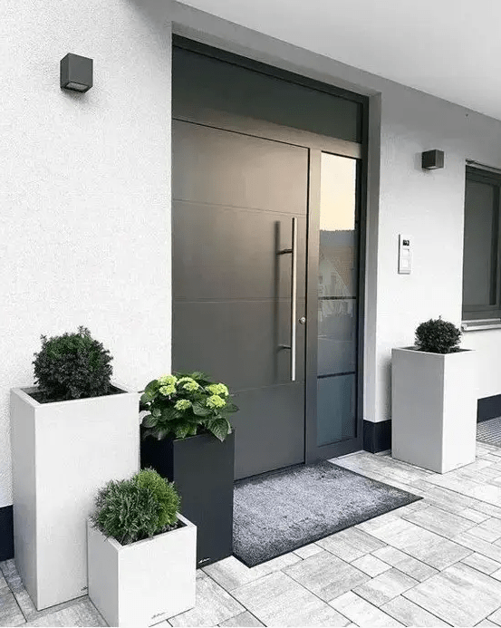 a modern to minimalist front porch with neutral and black square planters with greenery, a heavy black door and a rug