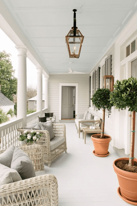 a neutral and welcoming summer porch with neutral wicker furniture, a wooden sofa, potted trees