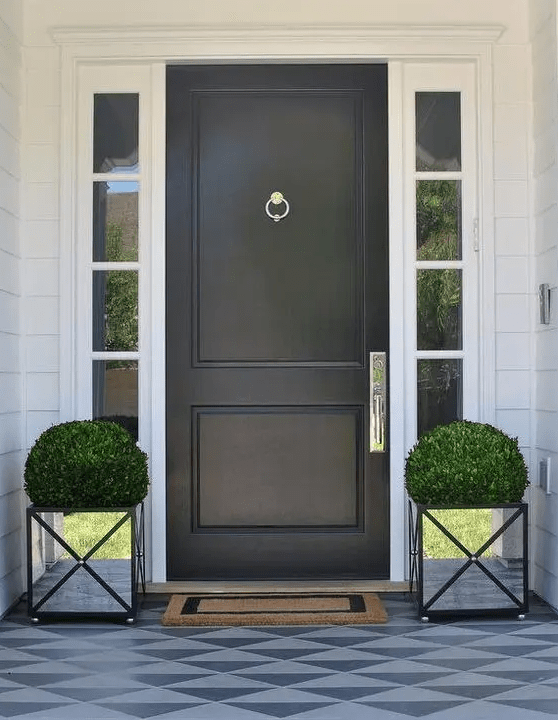 a refined modern entrance with a black door, glass panes and amirror planters with topiaries that add shine to the space