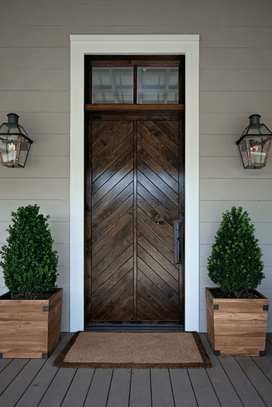 a refined porch with a stained wood door and wooden planters with boxwood for a rustic feel