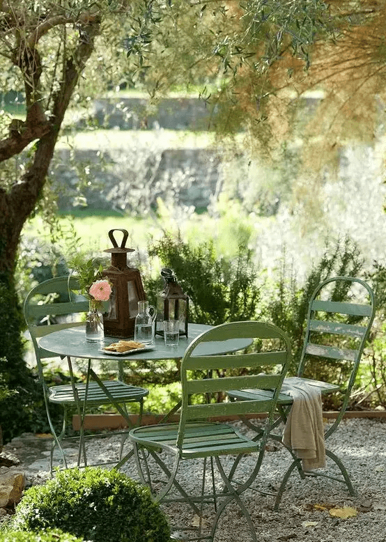 a small and cozy garden dining area with simple green metal furniture is located under the tree and is very inviting