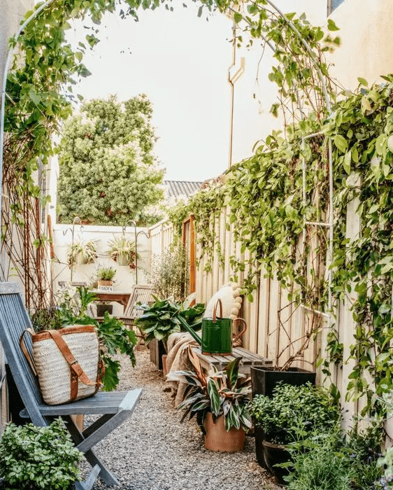 a small backyard turned into a secret garden with a living wall, some climbing plants and potted ones, a wooden dining set, some folding chairs