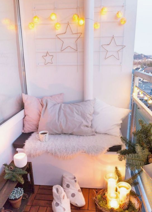 a small winter balcony with lots of lights, star decor, faux fur, pastel pillows, candles, pinecones and evergreens