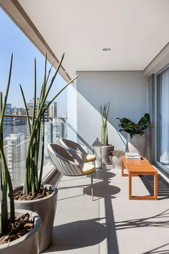 a stylish modern balcony with a brigth stained table, a couple of curved chairs, statement potted plants and a candle lantern