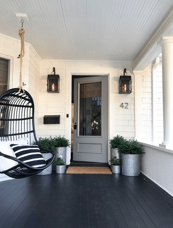 a stylish modern black porch with potted greenery in metal planters, a black suspended chair with graphic pillows and lanterns