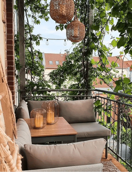 a stylish modern spring balcony with grey upholstered furniture, lots of greenery, woven pendant lamps and candle lanterns