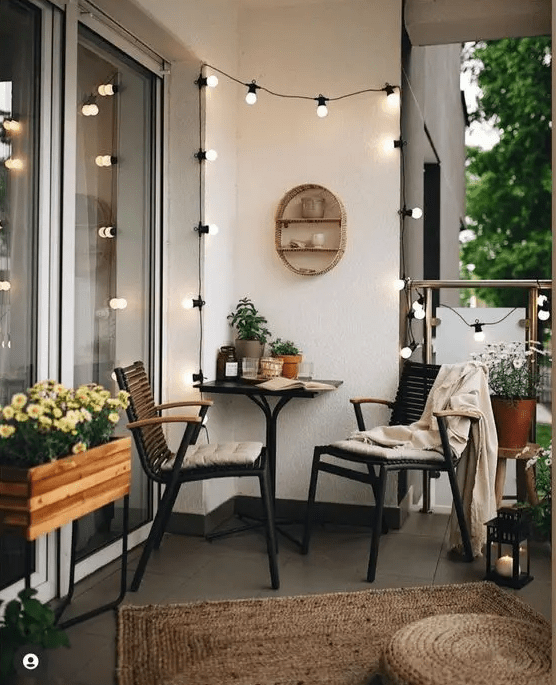 a stylish spring balcony with dark furniture, a table, potted blooms, lights and jute rugs and poufs