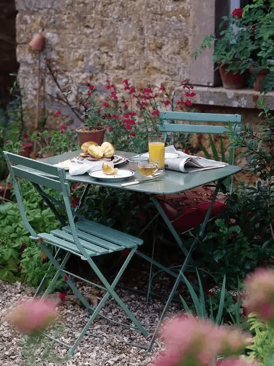 a very small and cute dining space with green metal furniture and chairs and lots of blooms around