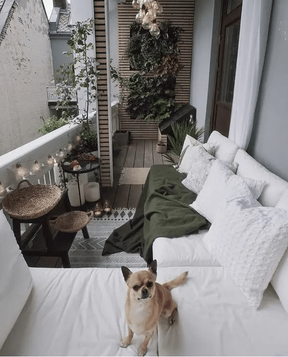 a white balcony with a corner seating, a stool with baskets, a stand wth floating blooms and candles