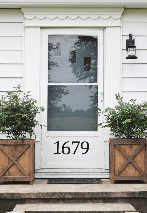 a white door with glass and a house number plus wooden planters and small trees for a vintage farmhouse feel