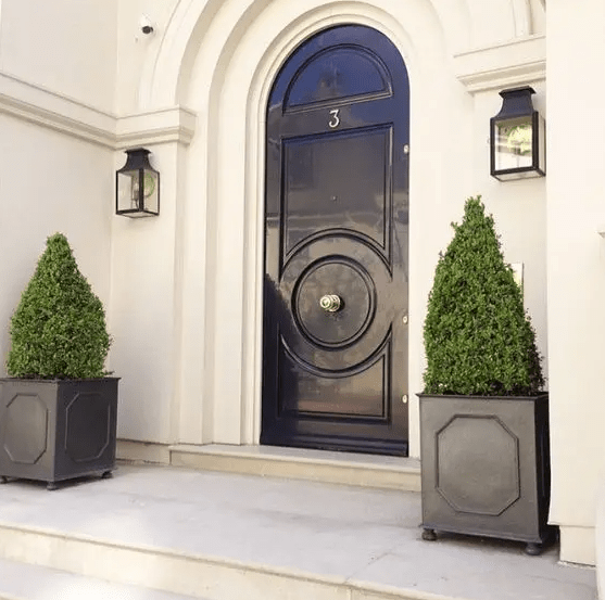 an elegant porch with a black front door, black planters with boxwood topiaries for a chic look and black wall sconces