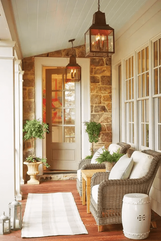 an elegant summer porch with wicker chairs and a coffee table, printed textiles, potted greenery and lanterns