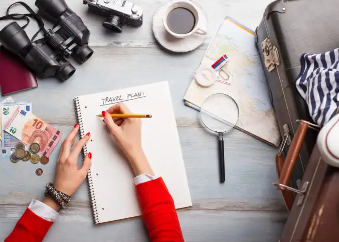 Overhead view of someone planning their trip in a notebook surrounded by travel items