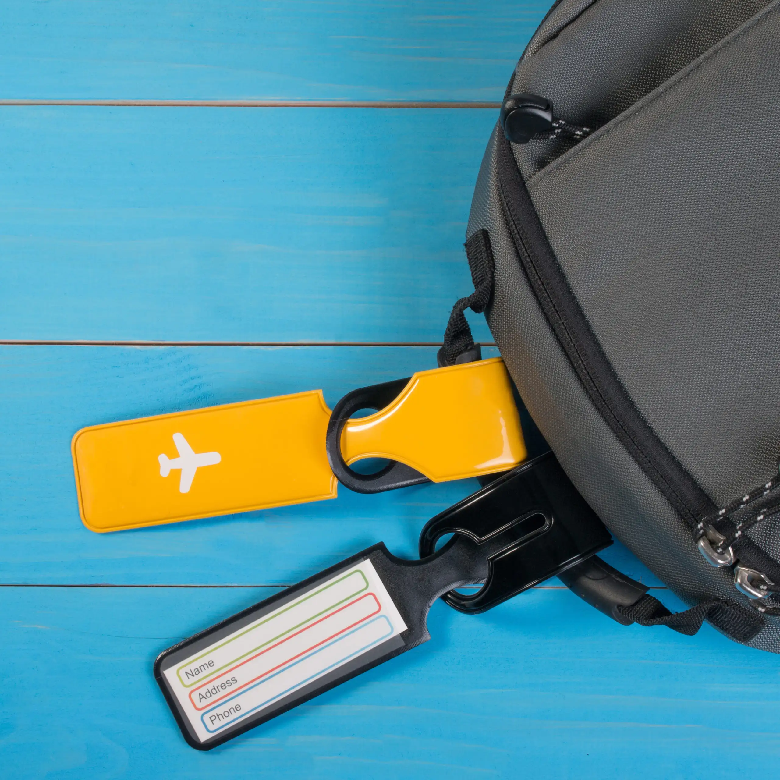 Grey bag with yellow and blue luggage tags, sitting on a bright blue table