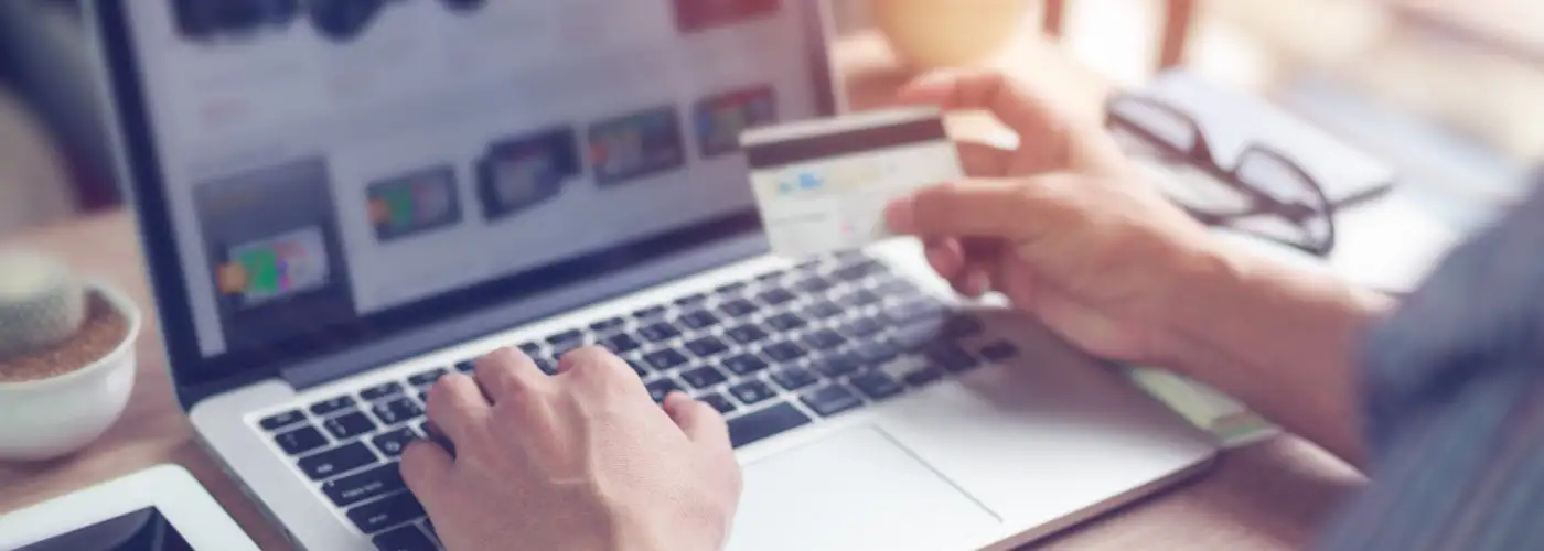 Close up of man's hands typing on a computer and holding a credit card