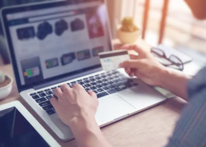 Close up of man's hands typing on a computer and holding a credit card